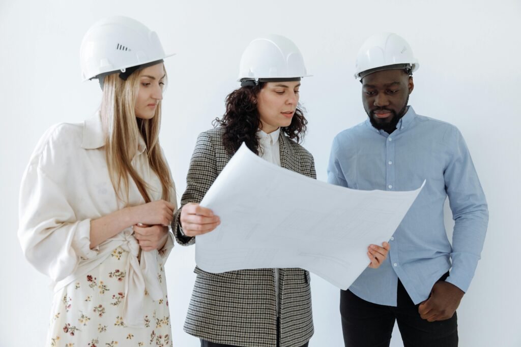Three architects wearing hard hats reviewing blueprints indoors for a construction project.